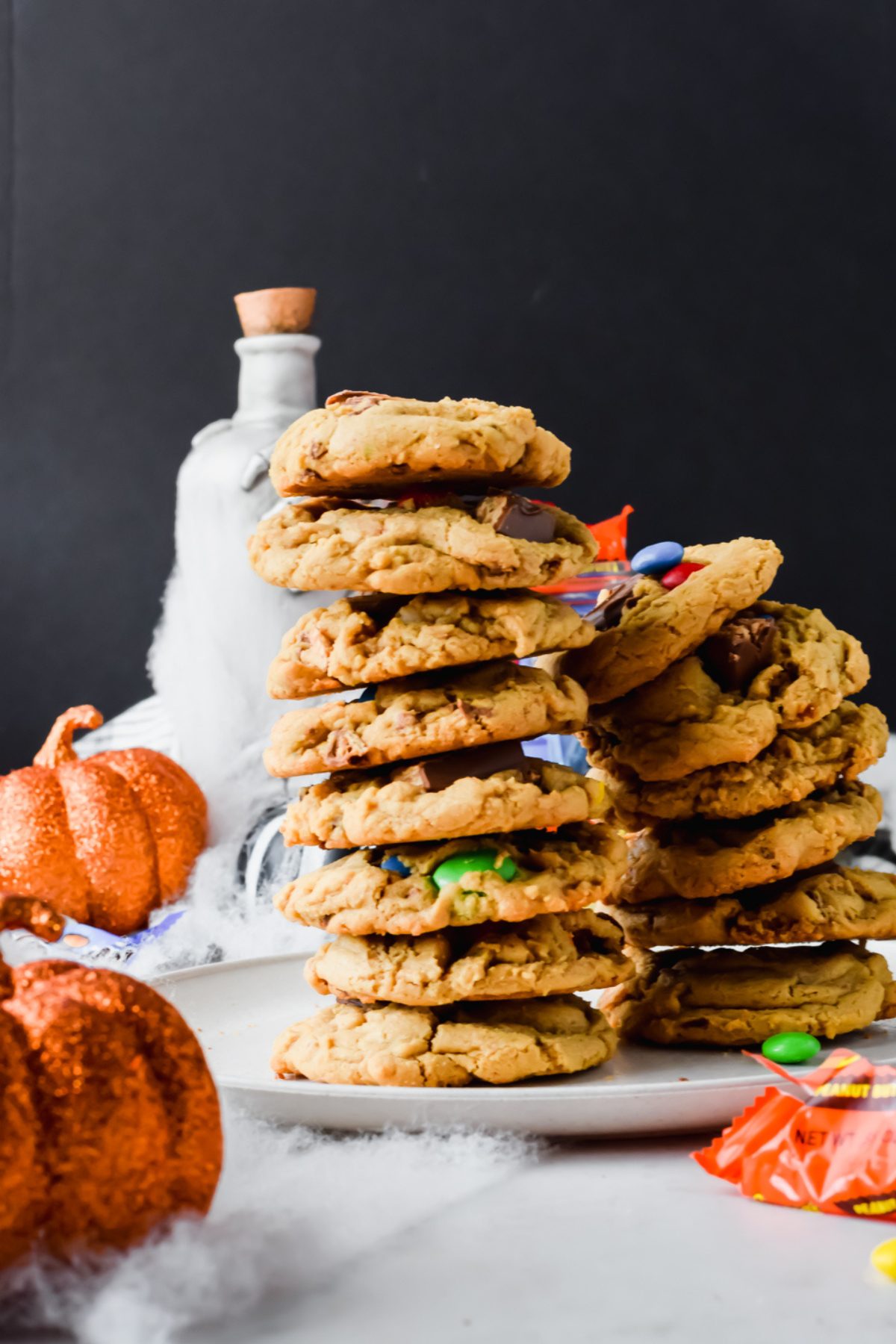 two stacks of leftover halloween candy cookies on white plate with halloween decor in background.