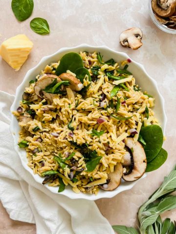 mushroom rice pilaf garnished with fresh mushrooms and spinach in white ceramic bowl on stone background.