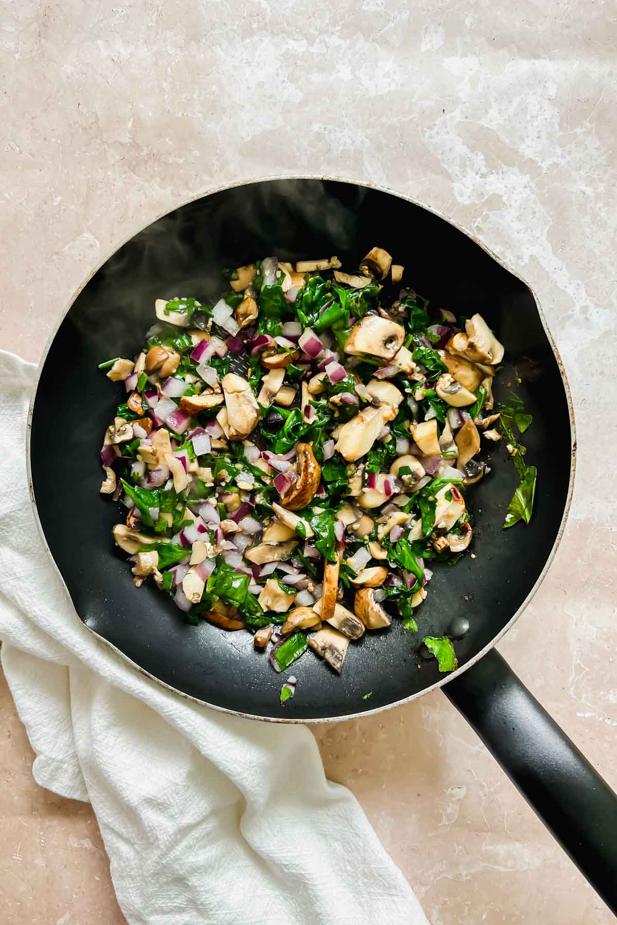saut&eacute;ed spinach, mushroom, onion, and garlic in a black skillet. 
