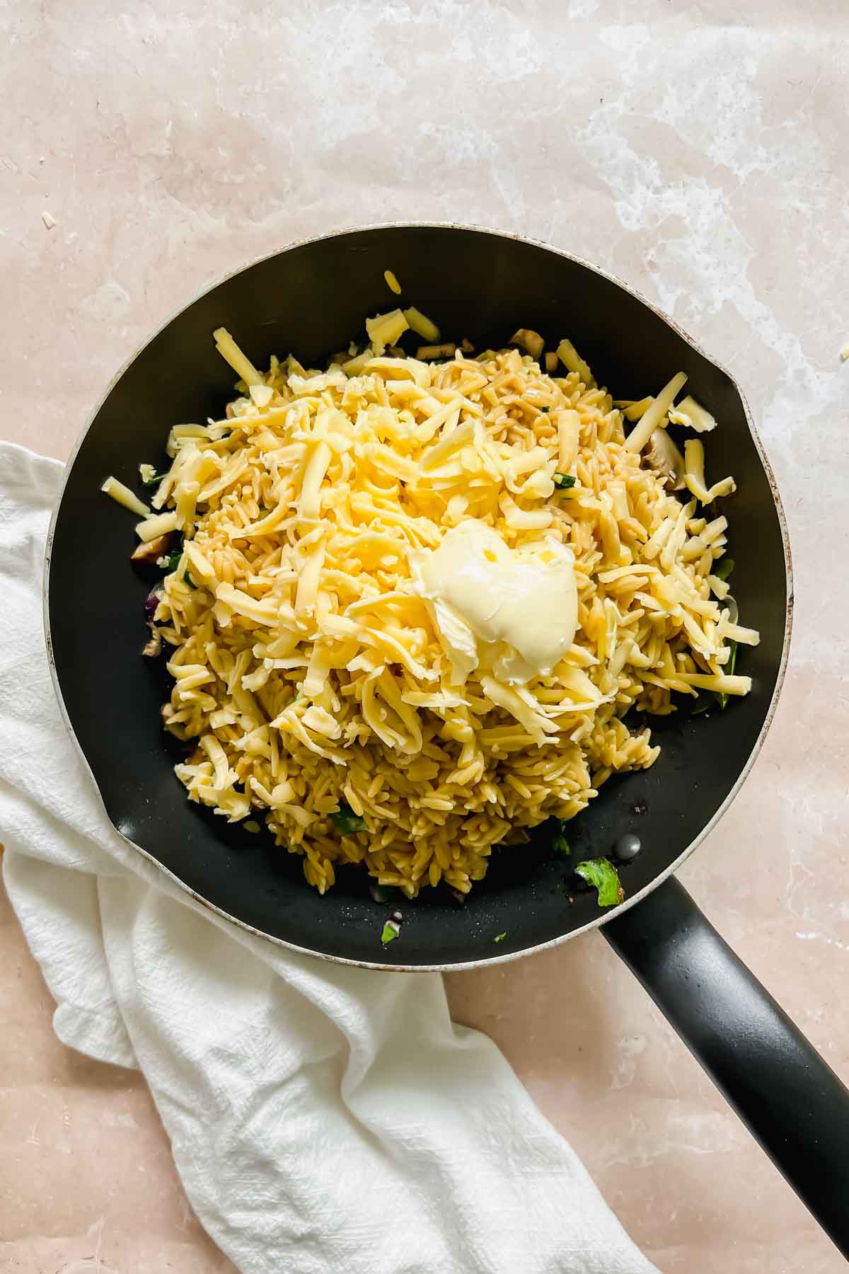 cooked rice added to the vegetable skillet with butter on stone background. 