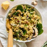 cooked mushroom rice pilaf garnished with fresh spinach and mushrooms with wooden spoon on stone background.