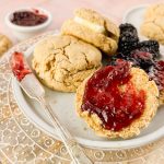 white plate of oat flour biscuits spread with raspberry jam.