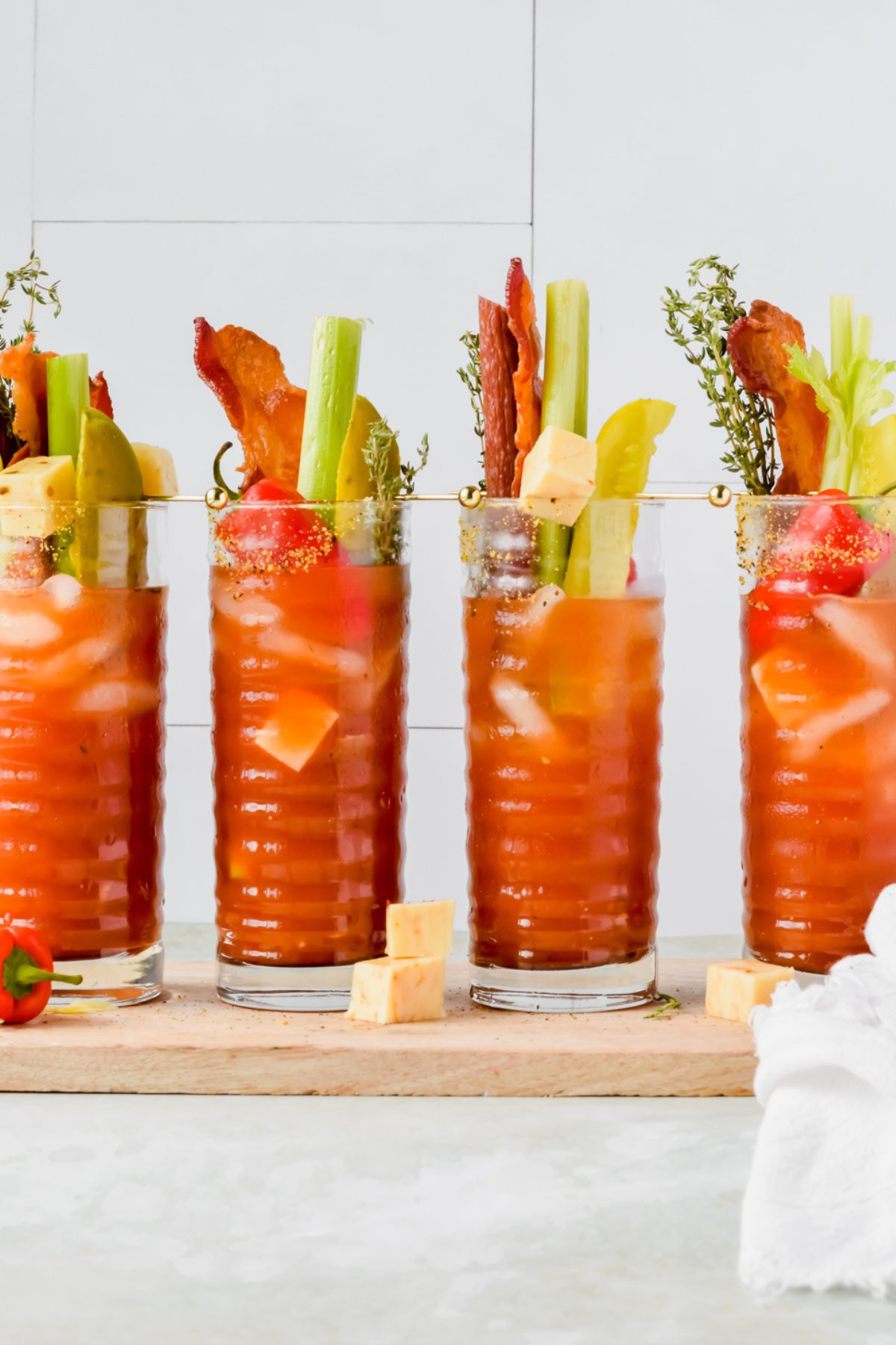four pickle bloody mary garnished with celery sticks, pickles, bacon, cheese cubes, and peppers.
