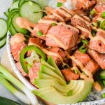 assembled spicy salmon bowl drizzled with spicy mayo beside additional recipe ingredients.