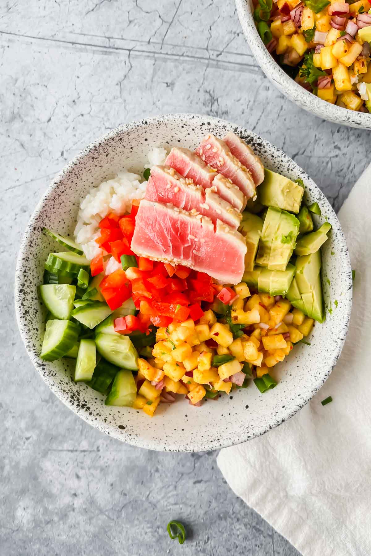 assembled ahi tuna rice bowl with fresh diced cucumber, red bell pepper, and avocado on top.