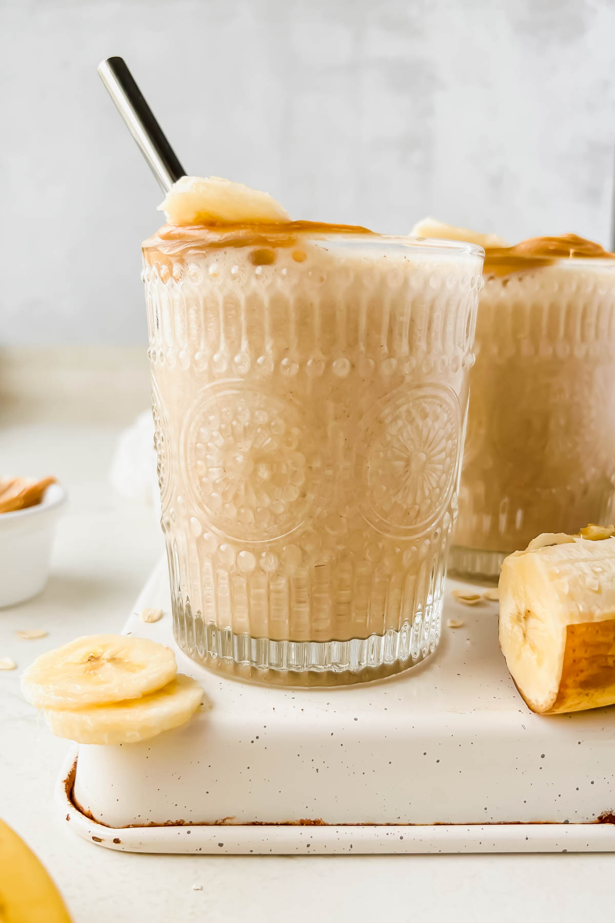two banana bread protein smoothies in glasses garnished with banana slice and a peanut butter rim.