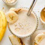 banana bread protein smoothie garnished with banana slice, peanut butter and rolled oats.