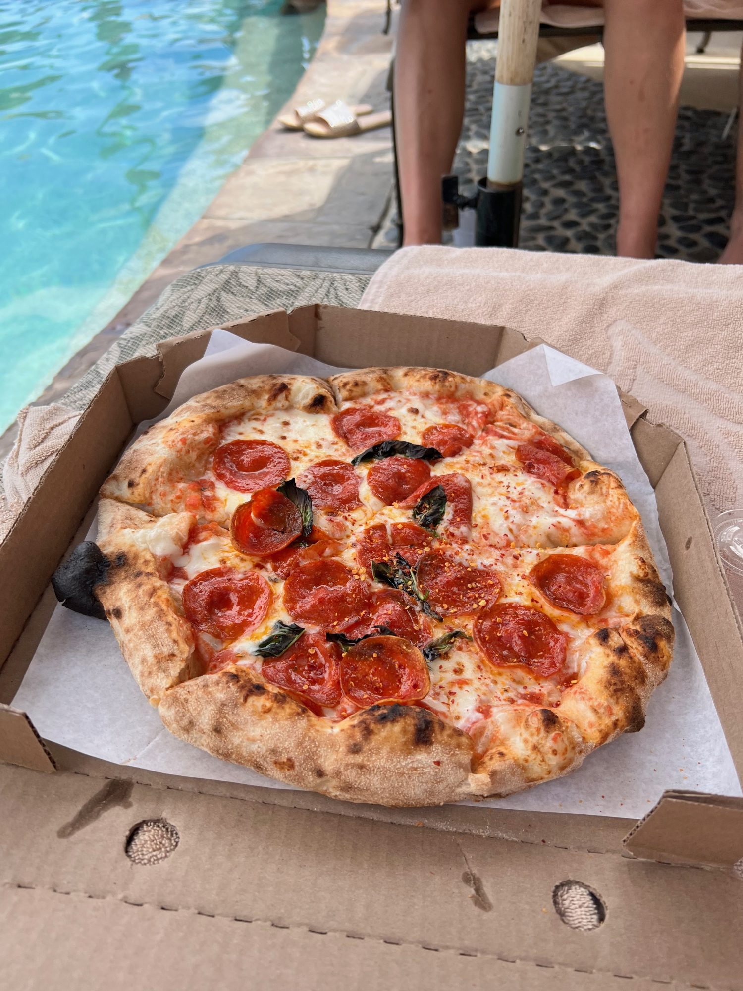 Tabasco's pizza in a brown box on a lawn chair next to the pool.