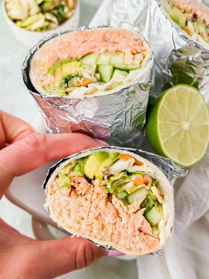hand grabbing california fish burrito sliced in half and wrapped in tinfoil.