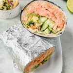 two california fish burrito halves wrapped in tinfoil stacked on top of each other on white plate.
