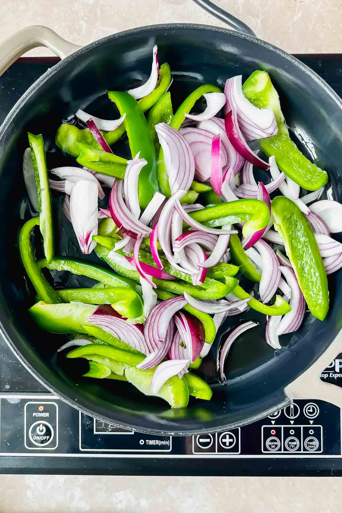 raw green bell peppers and sliced red onions in black skillet.