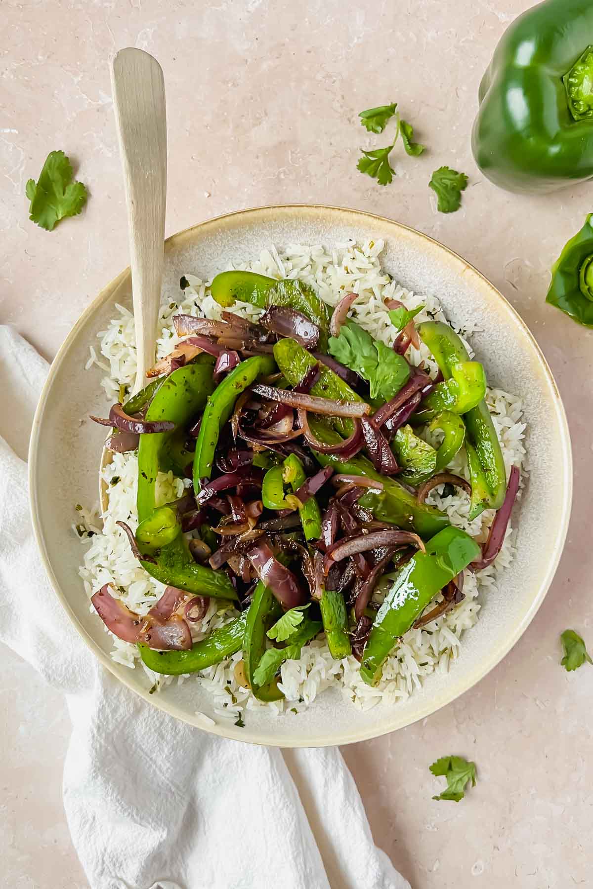 chipotle fajita veggies on top of plate of rice with spoon stuck in dish.