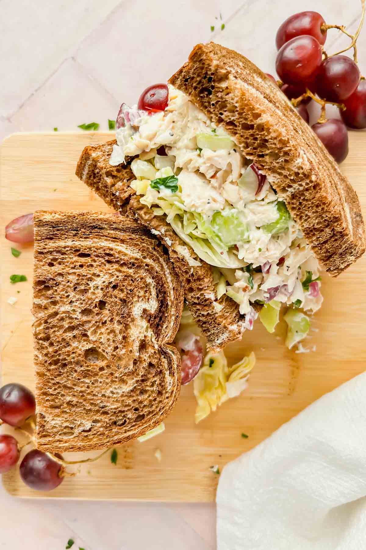 two halves of copycat panera bread chicken salad sandwich on brown bread stacked on top of eachother.