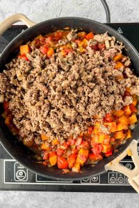 sweet potatoes, red bell pepper, white onion, tomatoes, and jalapeño sautéed in skillet with ground beef added on top.