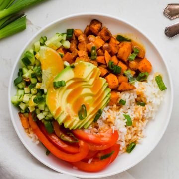 assembled vegan rice bowl garnished with green onion and spicy mustard dressing in white dish.