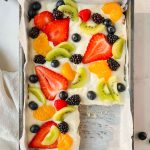 healthy gluten free fruit pizza garnished with fresh fruit in metal tray on white background.