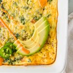 Baked Healthy Frittata in a white serving dish garnished with avocado and sauce.