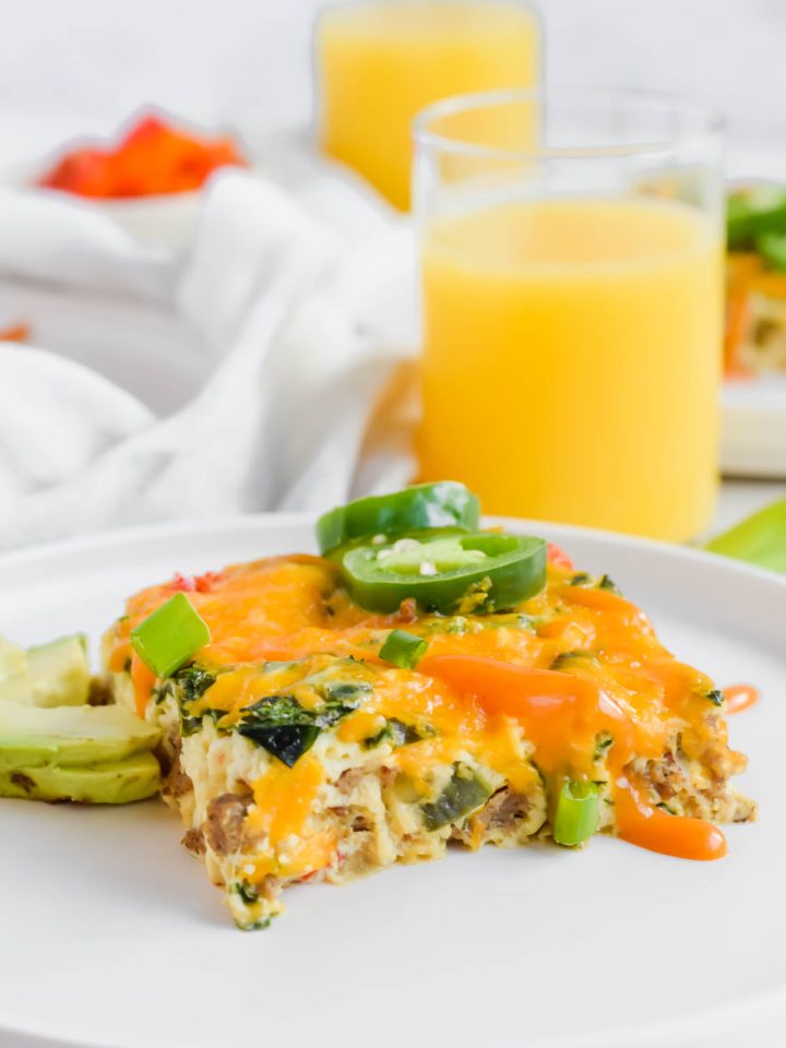 Slice of Healthy Frittata on white plate with sliced avocado and a glass of orange juice.