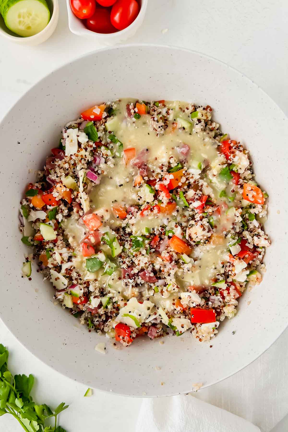 italian quinoa salad ingredients tossed in large mixing bowl topped with dressing.