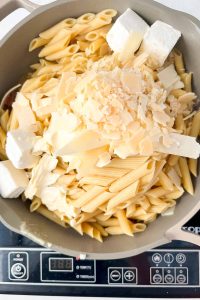 penne noodles in pot topped with cream cheese and shaved parmesan.