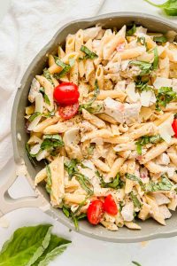 olive garden chicken pasta in gray skillet topped with fresh basil and cherry tomatoes.