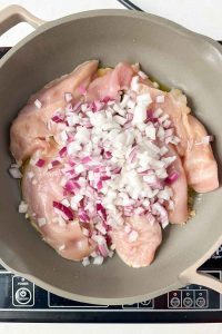 raw chicken breasts and diced onion cooking in gray skillet.