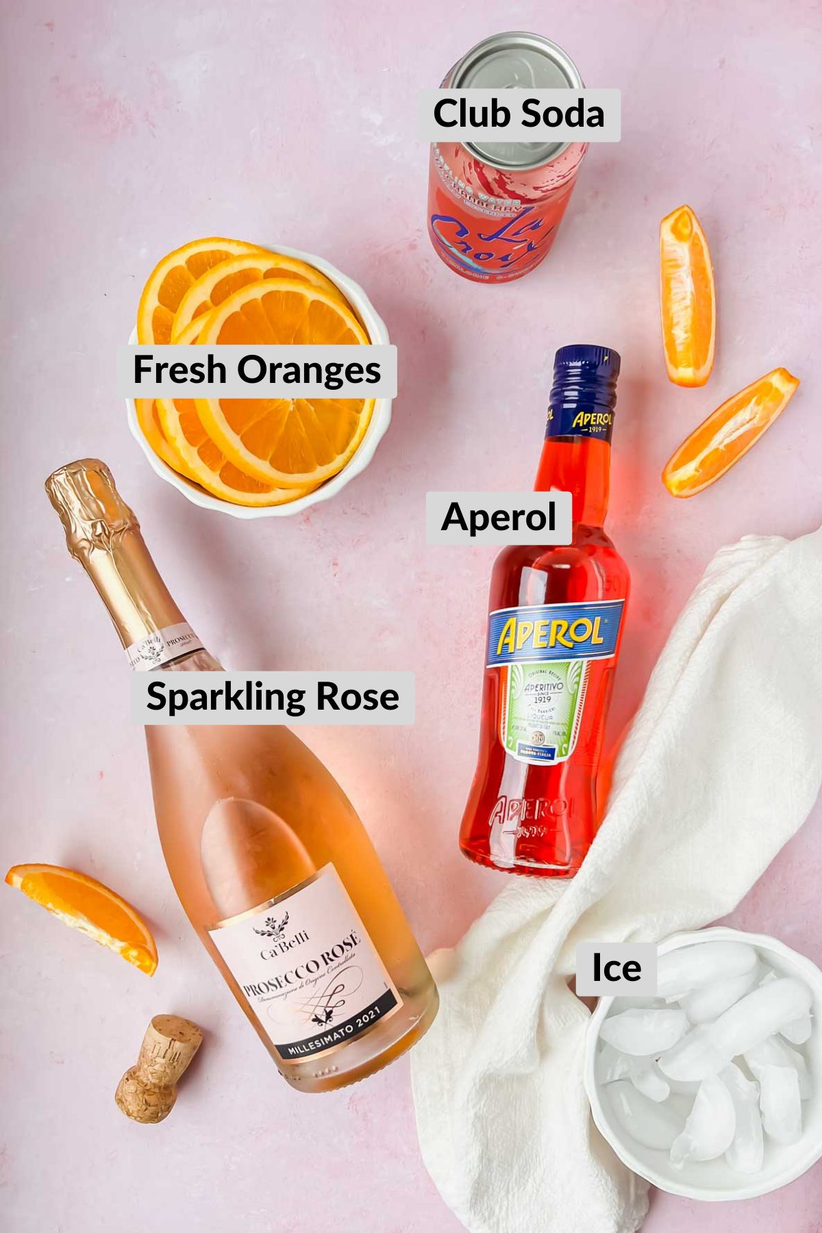 labeled rosé aperol spritz ingredients on light pink background.