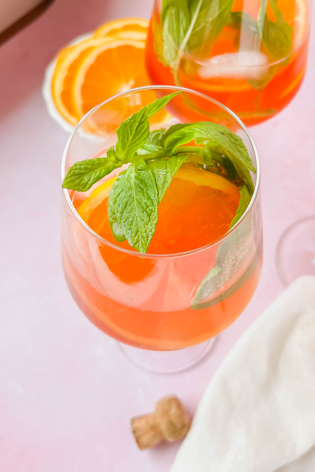 rosé aperol spritz in wine glass garnished with orange slices and mint leaves.