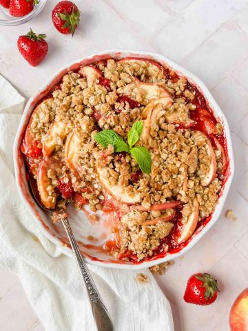 strawberry apple crisp baked to perfection with a golden crumble on top and a spoon serving it.