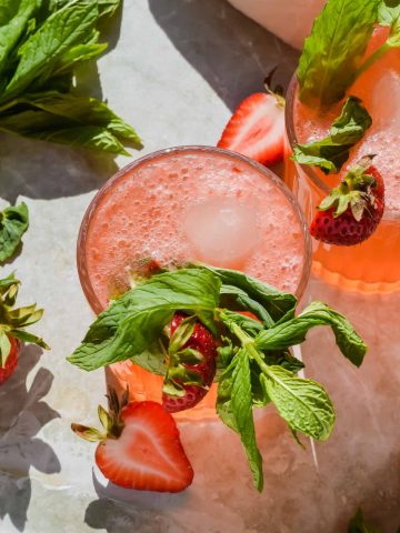 overhead view of two strawberry gin smash cocktails garnished with mint and fresh strawberry slices.