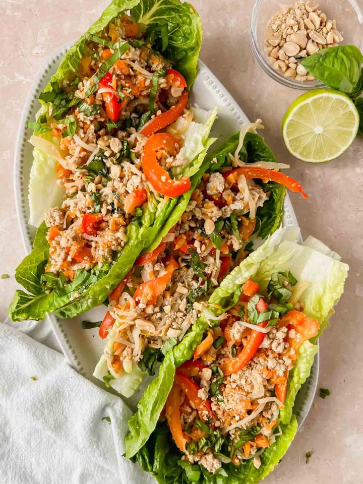 thai chicken lettuce wraps on white ceramic plate with light brown background.