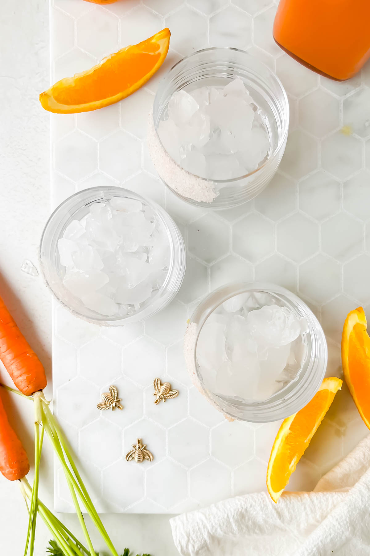 three cocktail glasses filled with ice surrounded by carrot margarita ingredients.
