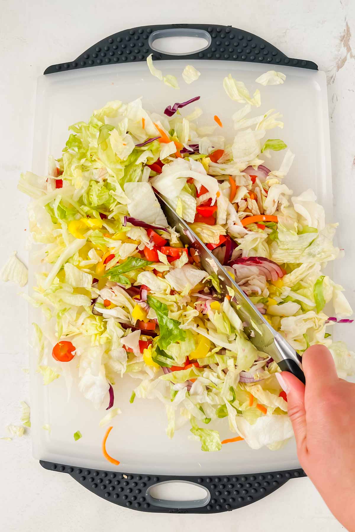 grinder chopped salad ingredients spread on white cutting board with knife chopping veggies.