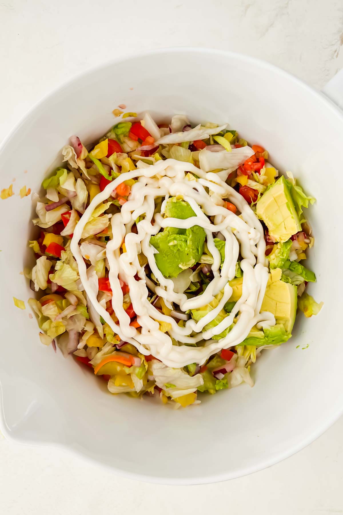 chopped grinder salad ingredients in white bowl topped with mayo.
