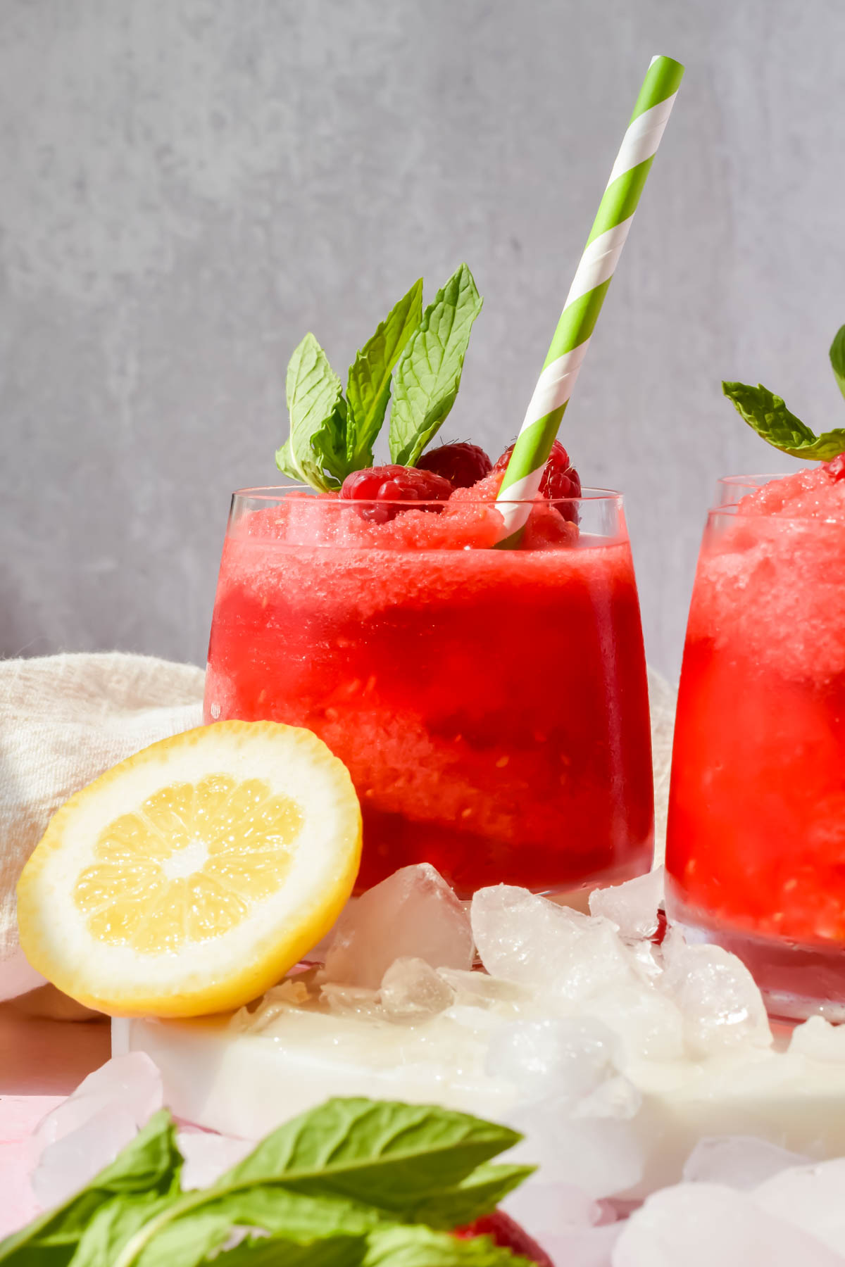 frozen raspberry lemonade refresher in glass garnished with fresh raspberries, mint leaves and straw.