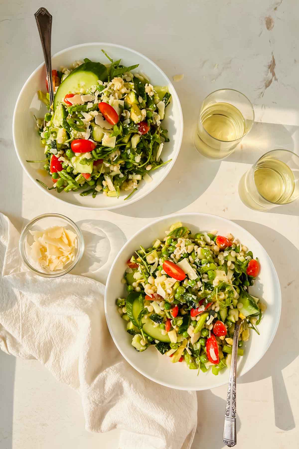 two white serving bowls filled with green summer salad.