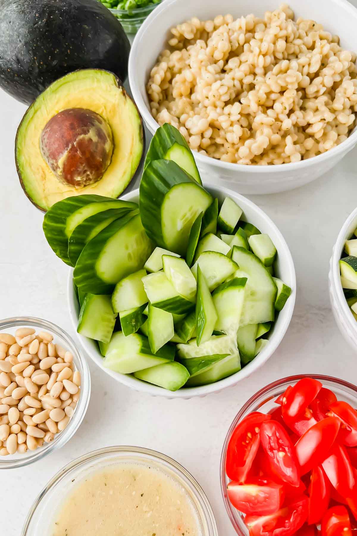 chopped cucumbers, pine nuts, couscous, tomatoes, and dressing in individual bowls.