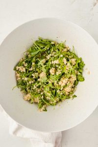 couscous and arugula in large white mixing bowl.