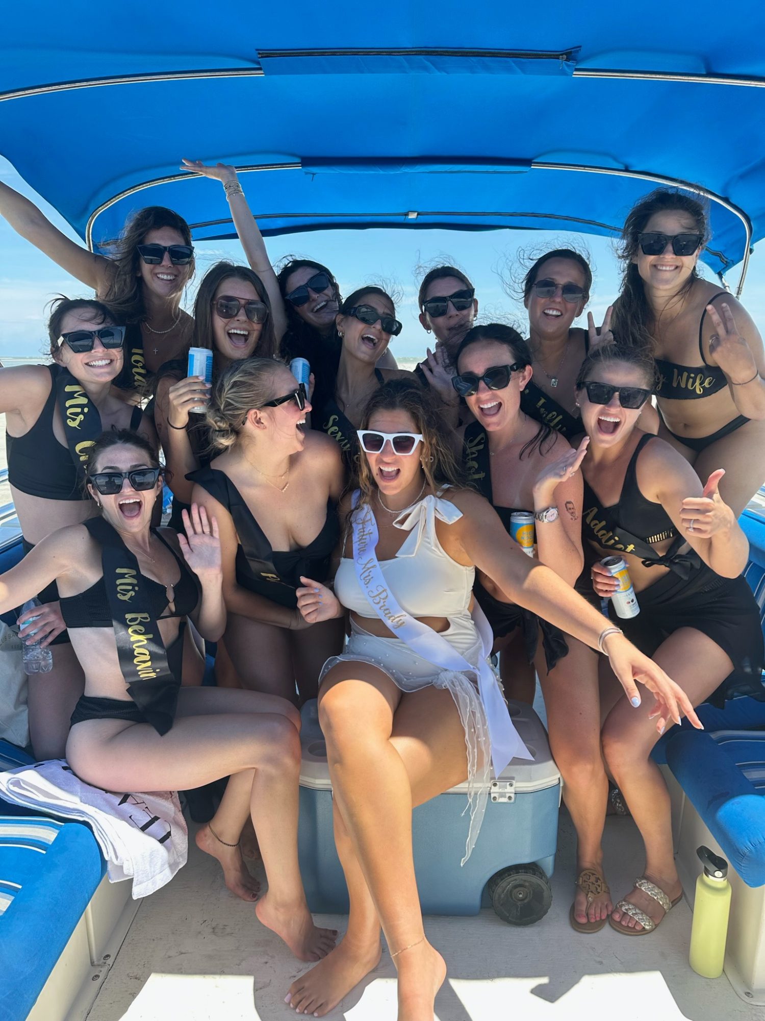 13 girls on a pontoon boat in matching black bathing suits and srongs. 