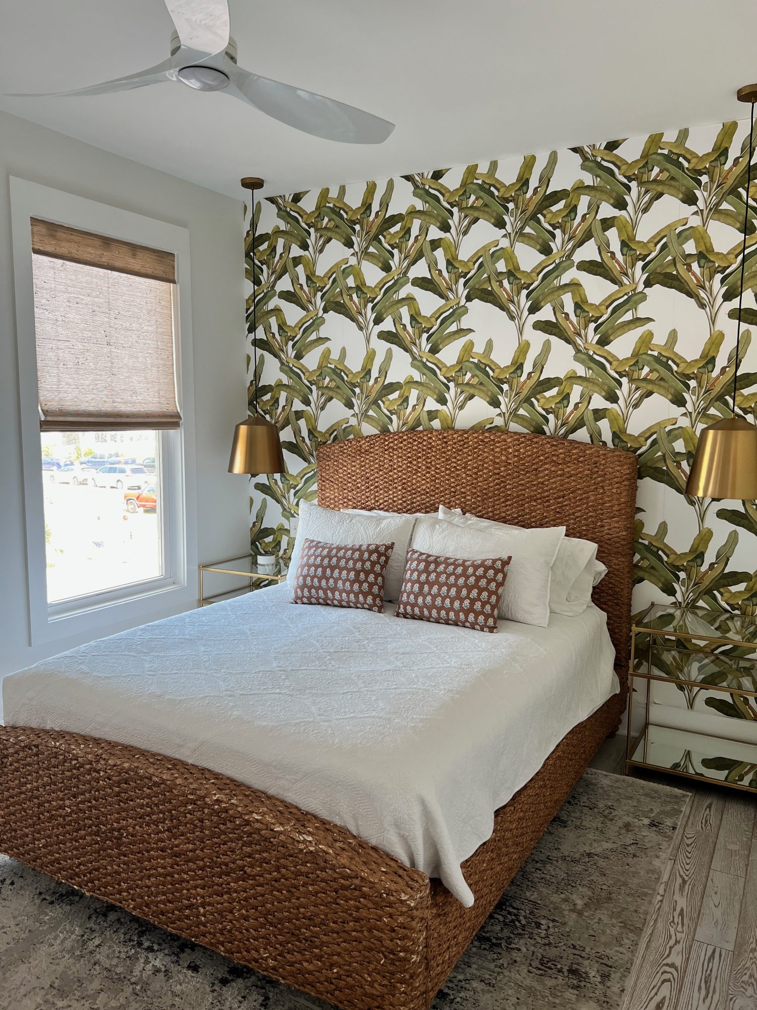 white linen bed with whicker bed frame on wall with palm tree wallpaper.