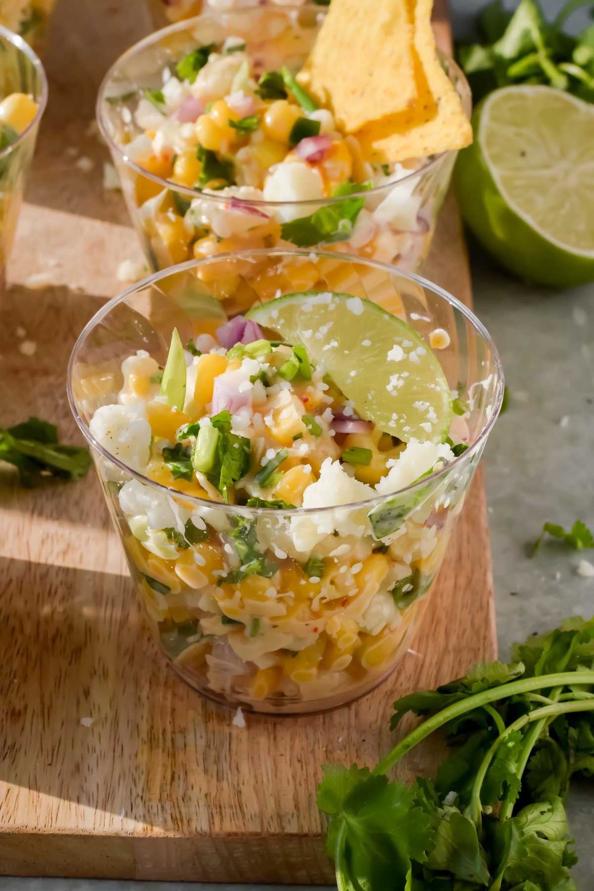 elote in a small glass cup with a lime wedge on top.