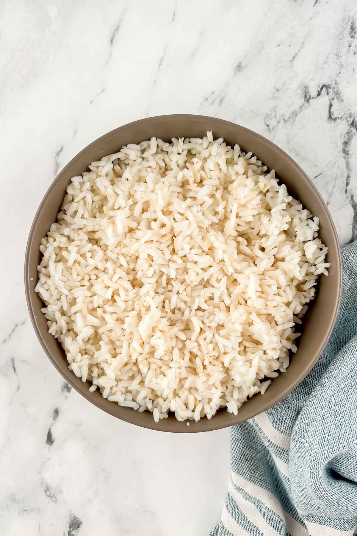 White rice in tan bowl on marble background.