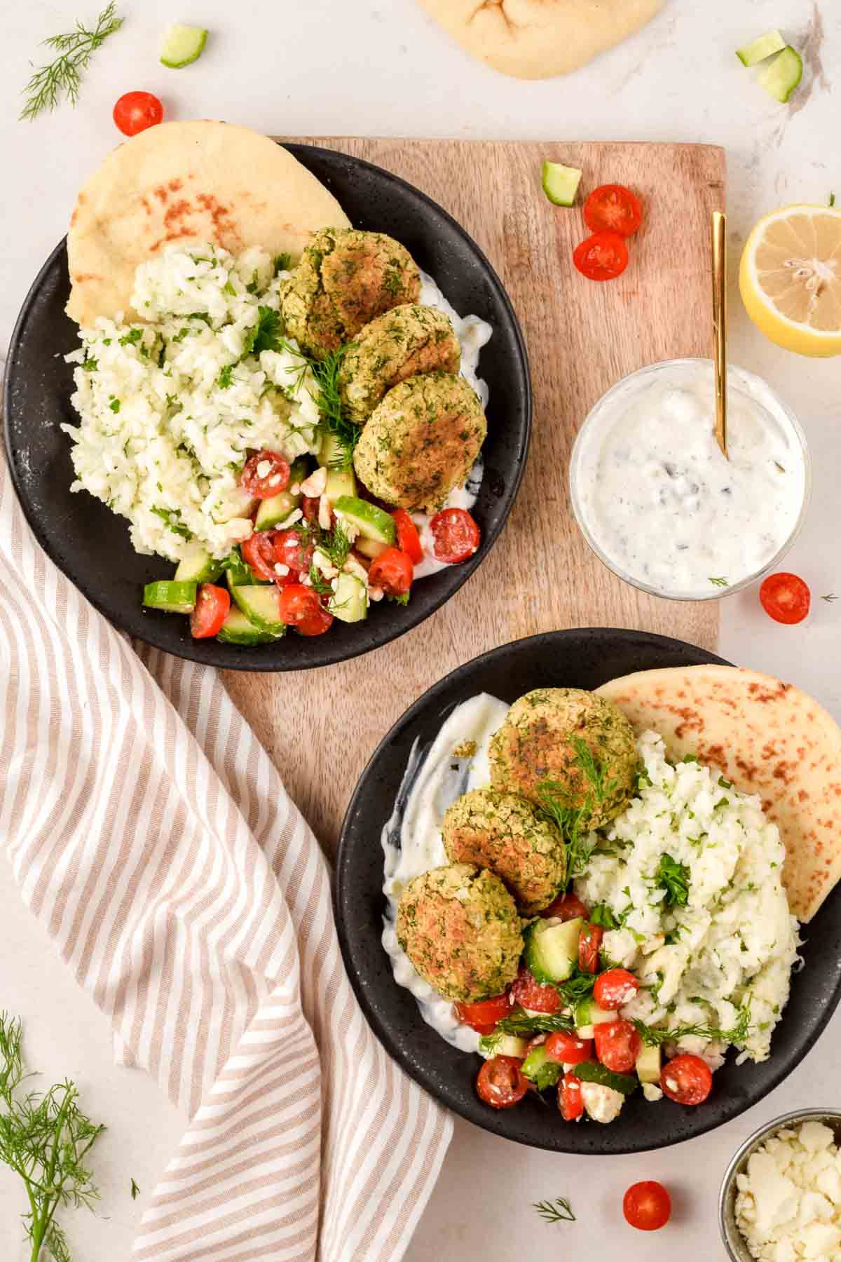 two falafel rice bowls garnished with cucumber and tomato salad and served with pita.