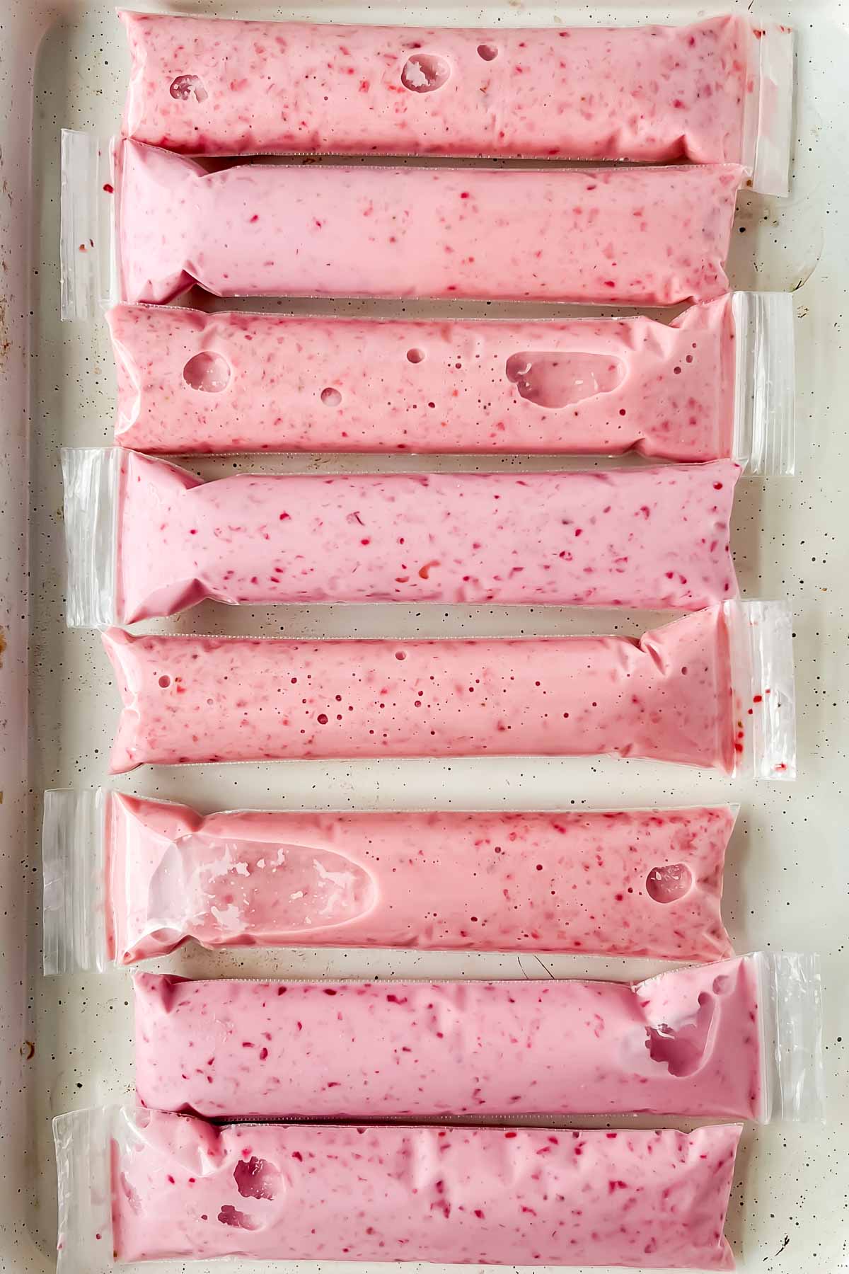 strawberry yogurt frozen in in plastics tubes on white baking tray.