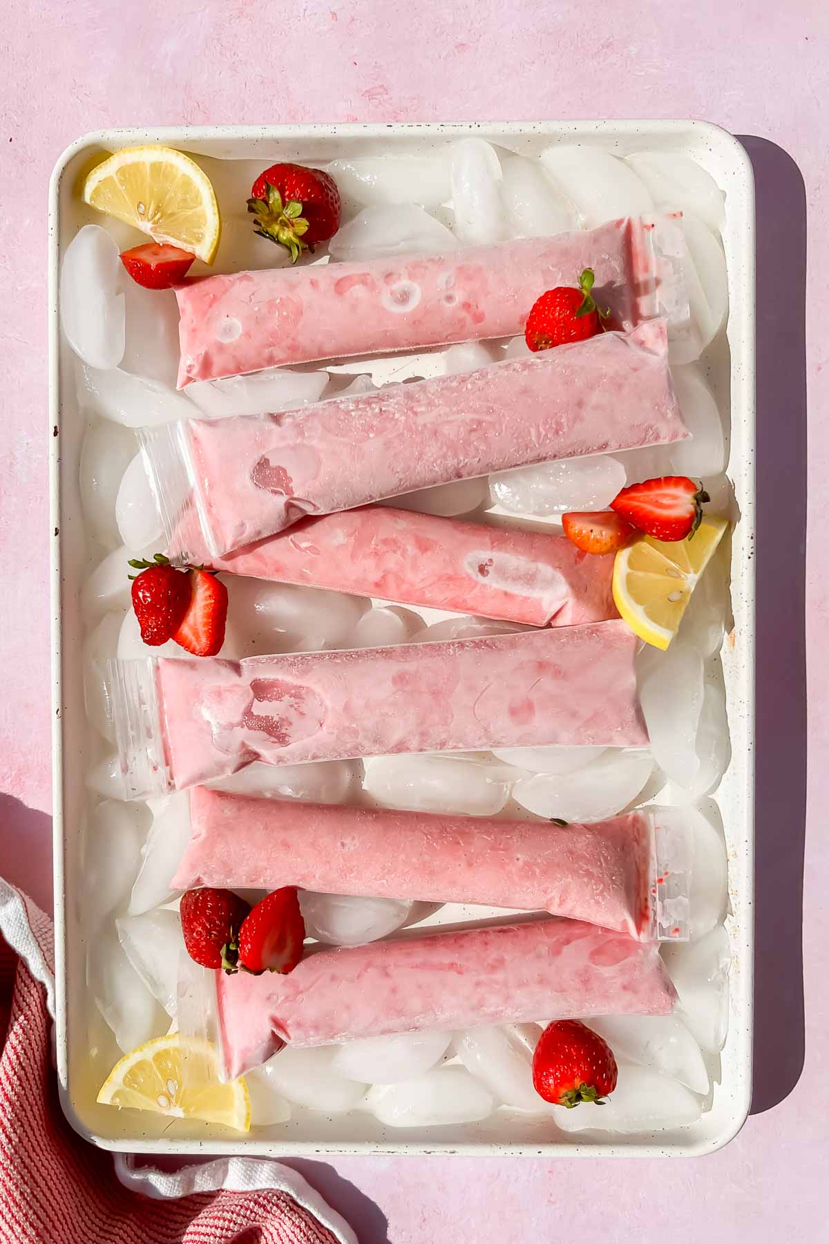 frozen yogurt tubes on ice on white baking tray.