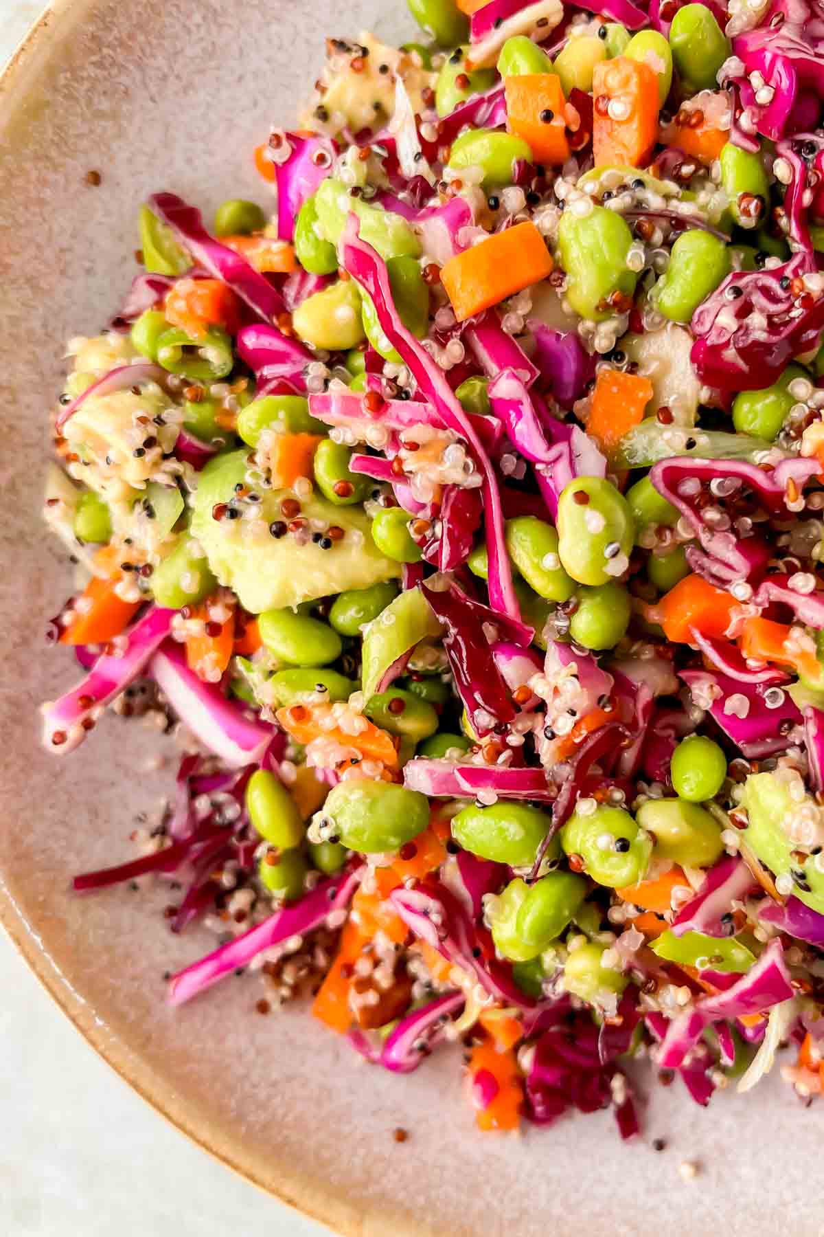 close up of quinoa edamame salad garnished with cabbage, carrots, edamame, and avocado. 