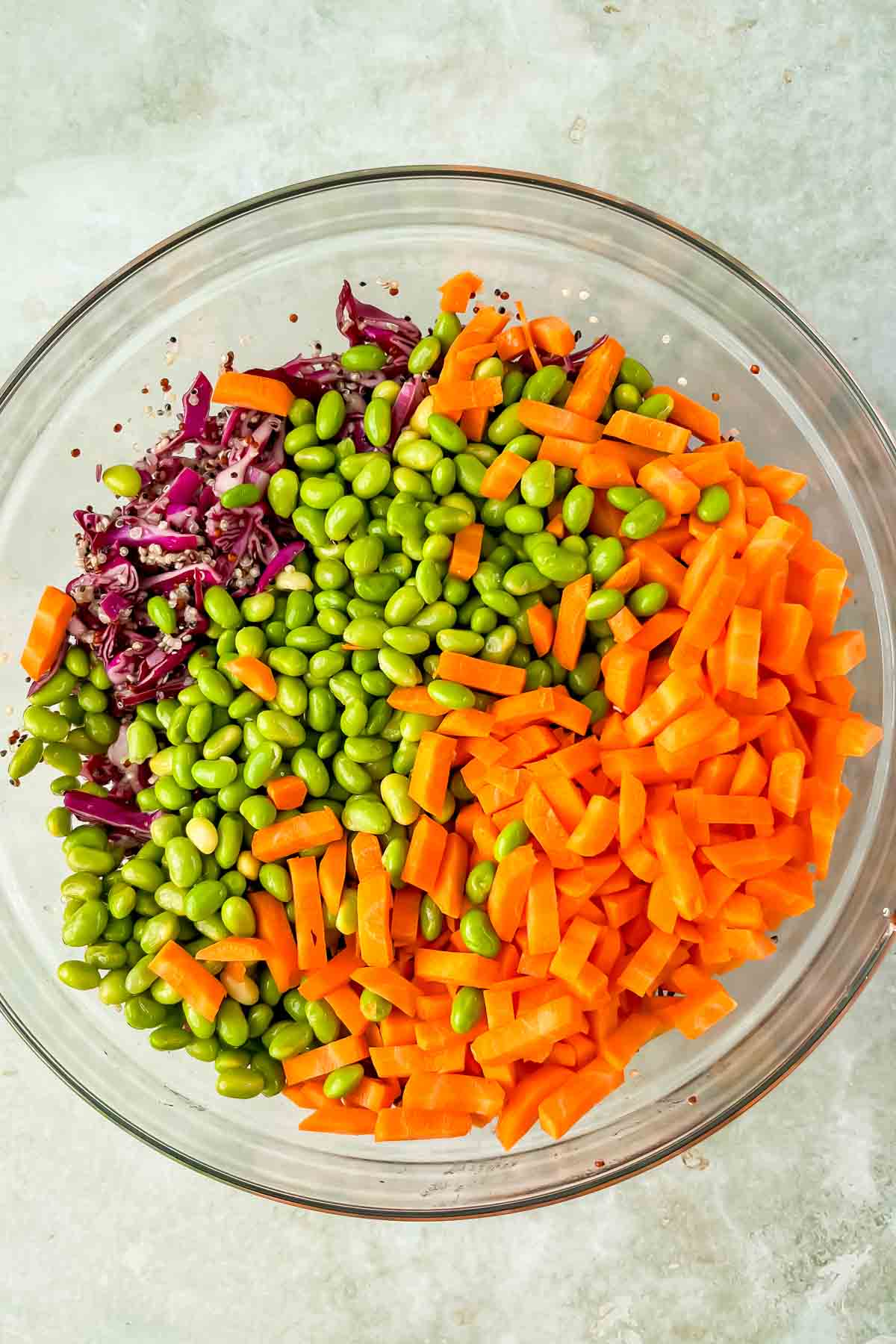 diced carrots, cooked edamame, shaved cabbage in glass mixing bowl. 