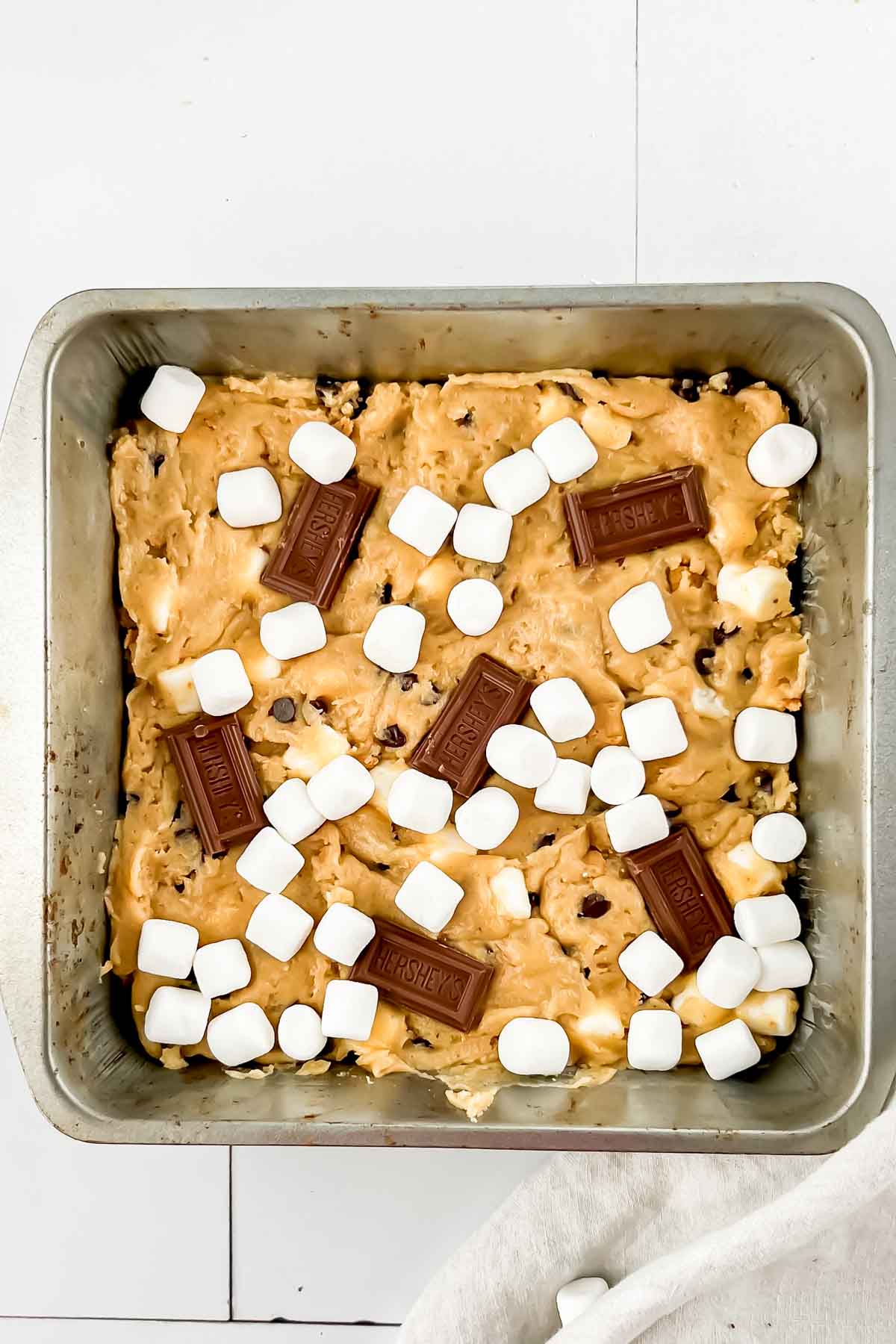 Smores casserole in square pan before baking topped with hersheys squares and marshmallows on top.