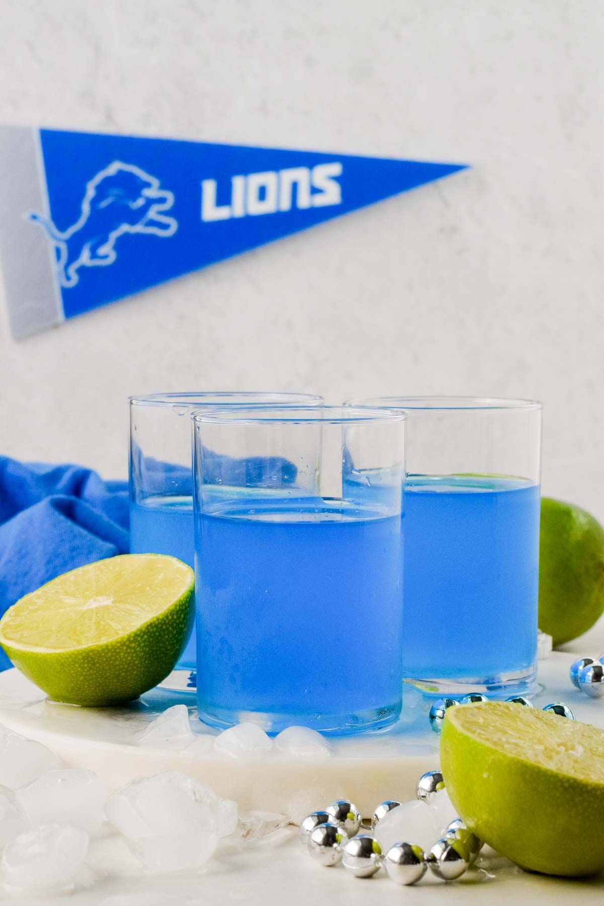 three blue kamikaze shots in glasses garnished with lime wedges and Detroit's Lions banner in the background. 