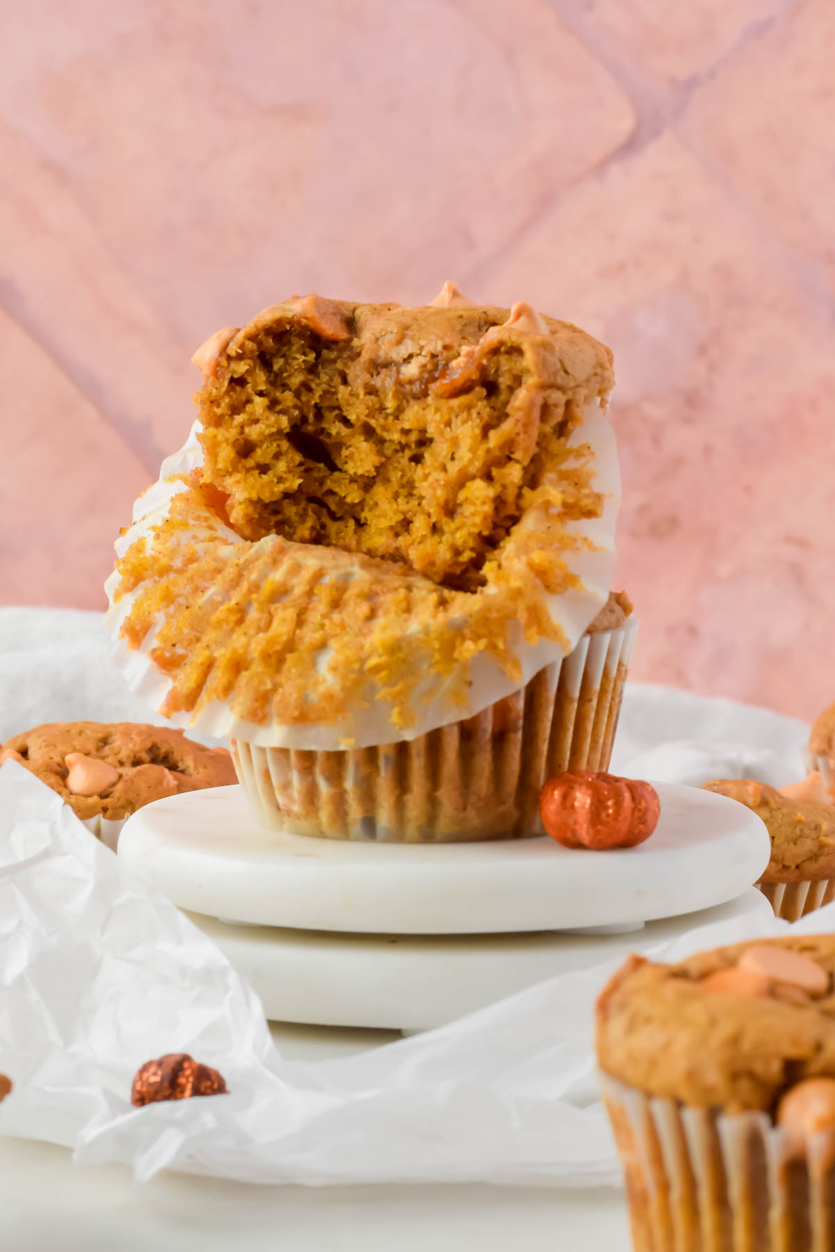 two stacked butterscotch pumpkin muffins with a bite out of the top one on white coasters.